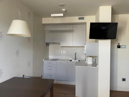 uma cozinha com armários brancos, uma mesa e uma televisão em Guiana Rooms - Adults Only em Ponferrada