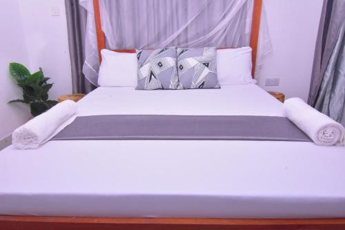 uma cama com lençóis brancos e almofadas em Volume view Apartments em Mombasa