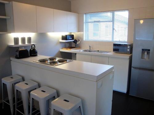 Una cocina blanca con encimera y taburetes. en Overbeek 1 Bedroom 702 Apartment on Kloof Street, en Ciudad del Cabo