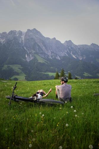 a man and a woman sitting in a field with a bike at Holzhotel Forsthofalm in Leogang
