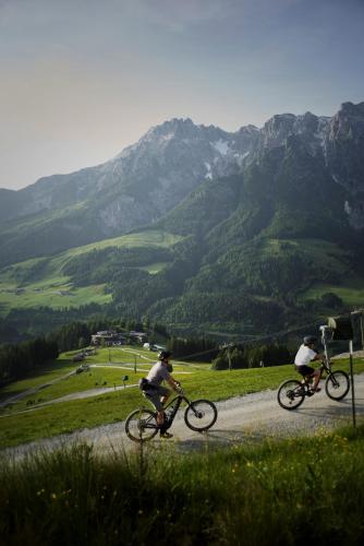 two people riding bikes on a gravel road with mountains at Holzhotel Forsthofalm in Leogang