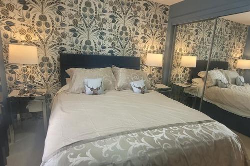 a bedroom with a large bed with two lamps and wallpaper at River walk Cottage in Kincardine OʼNeil