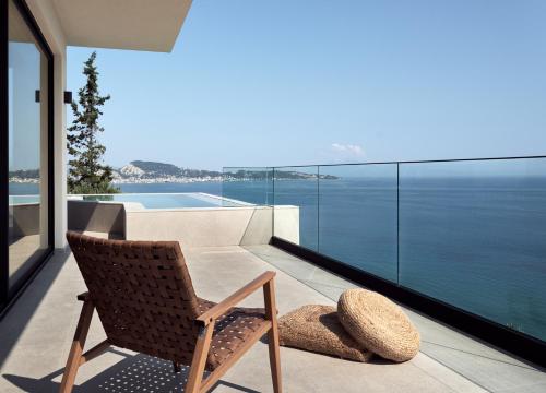 a chair on a balcony with a view of the ocean at Bardo Villa, Endless Blue with Heated Pool, By ThinkVilla in Argasi