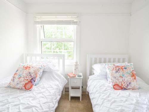 two white beds in a room with a window at River Lym Cottage in Lyme Regis