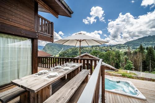 une terrasse en bois avec une table et un parasol dans l'établissement Chalet Cipolin Morzine - by EMERALD STAY, à La Côte dʼArbroz