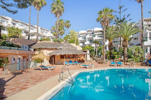 a swimming pool in a resort with palm trees and buildings at Apartamento en complejo con piscina, pádel y restaurante con vistas al golf en Mijas - Matchroom 83 in Fuengirola