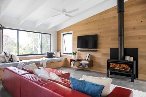a living room with a red couch and a fireplace at Bawley Beach House, Short Walk to Bawley Beach in Bawley Point