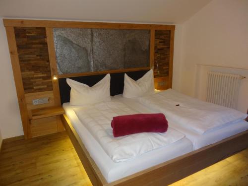 ein großes weißes Bett mit einem roten Kissen darauf in der Unterkunft Albingers Landhaus in Balderschwang