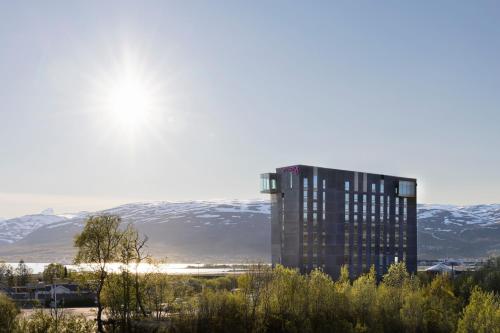 a tall building with snow covered mountains in the background at Moxy Tromso in Tromsø