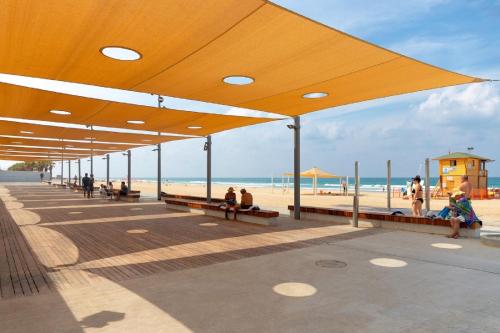 un paseo marítimo con gente sentada en bancos en la playa en דירת 4 חדרים מול הים, en Bat Yam