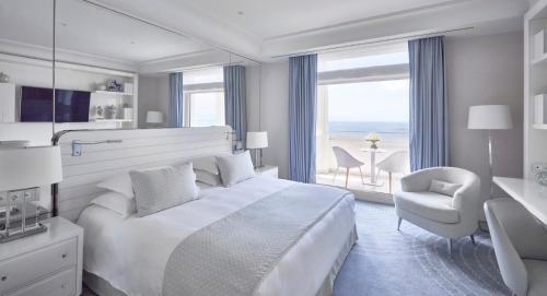 a white bedroom with a large bed and a chair at Hôtel Martinez, in The Unbound Collection by Hyatt in Cannes