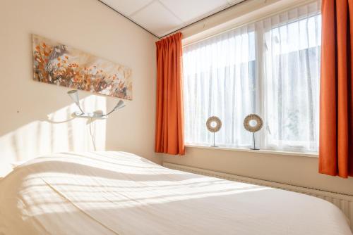 a bedroom with orange curtains and a bed and a window at Appartement Zuiderstrand in Zoutelande