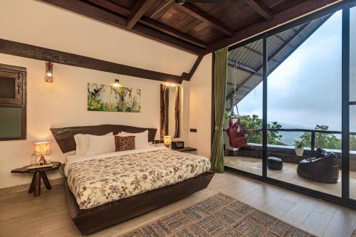 a bedroom with a bed and a large window at SaffronStays Aranya Vilas & Raanwaara Cottage in Āmbavna