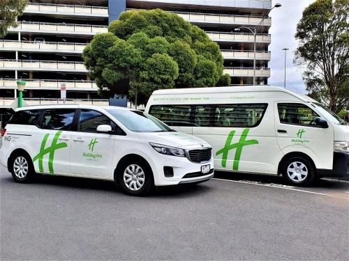two white vans are parked in a parking lot at Holiday Inn Melbourne Airport by IHG in Melbourne