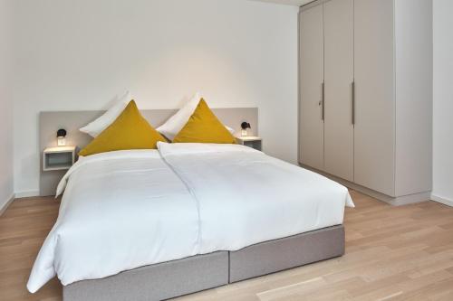 - une chambre blanche avec un grand lit blanc et des oreillers jaunes dans l'établissement Lüttjeod Apartmentvilla Lüttjeod Apartmentvilla 03, à Langeoog