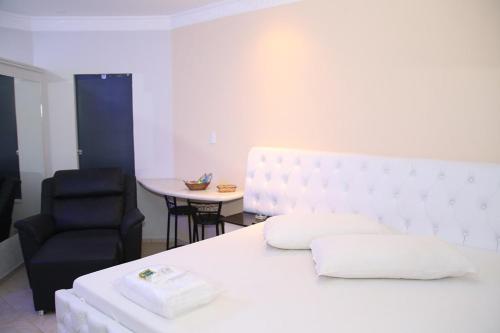 a bedroom with a white bed and a black chair at SAFIRA MOTEL II in Fernandópolis