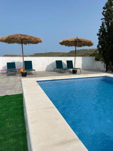 a swimming pool with two chairs and umbrellas at Casa rural con piscina climatizada y barbacoa a 10 km de Alicante y playas, 3000 m2 de terreno in Elche