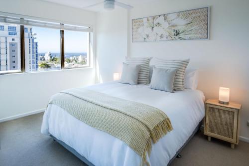 a white bedroom with a large bed and a window at Retro Style Apartment Kings Beach with Ocean Views in Caloundra