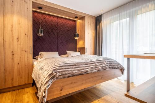 Dorfkrug Kaprun - Luxury Suites & Appartements by SFL في كابرون: غرفة نوم بسرير مع جدار خشبي