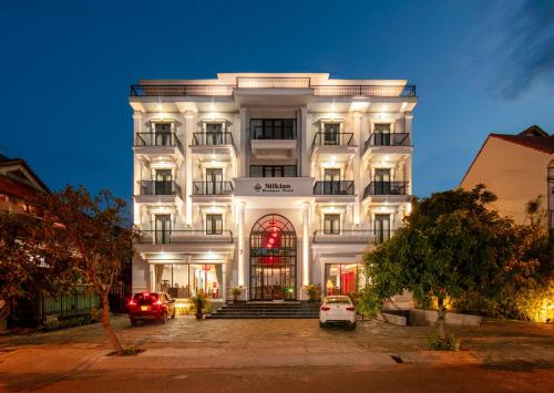 会安Silkian Hoian Boutique Hotel & Spa的一栋白色建筑，前面停着汽车