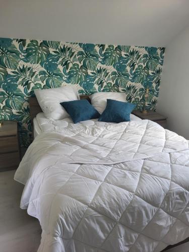 a white bed with blue pillows in a bedroom at L'escale des roses in Doué-la-Fontaine