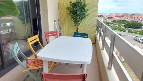a white table on a balcony with colorful chairs at Grand Studio 3 étoiles - Mimizan-Plage - 1 à 4 pers - Tout confort - 6 mn à pieds de la plage in Mimizan