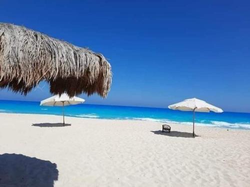 two umbrellas and a chair on a beach with the ocean at قريه ديمورا ك٧٥ الساحل الشمالي in Dawwār Abū Duray‘ah ‘Abd al Karīm