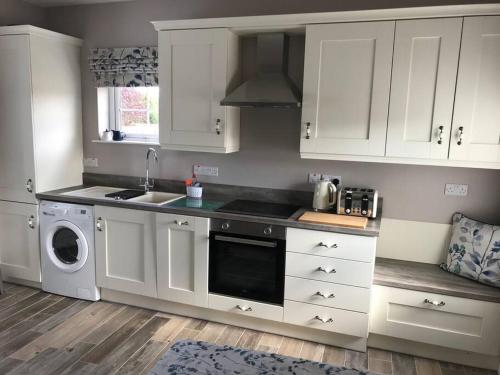 a kitchen with white cabinets and a sink and a dishwasher at Cosy Nook Cottage Kesh in Kesh