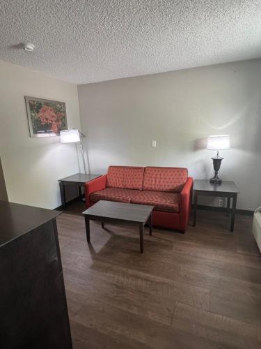 a living room with a red couch and two tables at Days Inn & Suites by Wyndham Monroe in Monroe