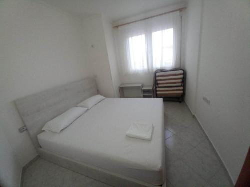 een wit bed in een witte kamer met een raam bij Appartamento per vacanze estive in Vlorë