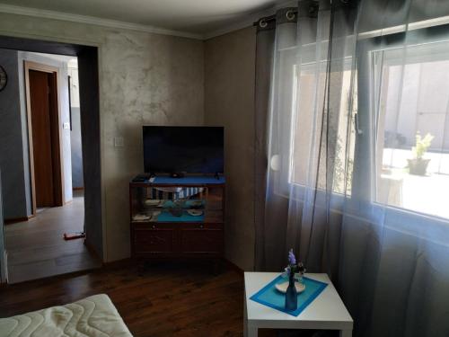 ein Wohnzimmer mit einem TV, einem Tisch und einem Fenster in der Unterkunft Studio Kaća in Cetinje
