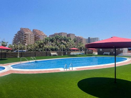 una gran piscina con césped verde y sombrilla roja en Apartamento Torremar M, en El Borseral