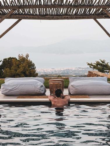 a man laying in a swimming pool next to beds at Three Dots Boutique Suites in Soúlion
