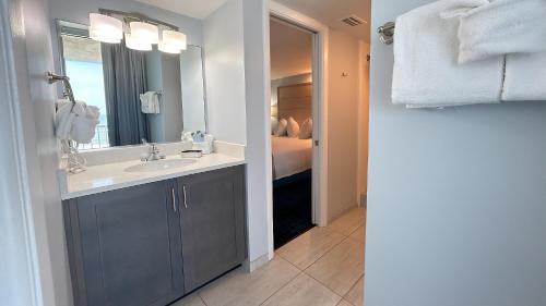 a bathroom with a sink and a mirror and a bed at Ocean East Resort Club in Ormond Beach