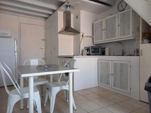 une cuisine avec des armoires blanches et une table et des chaises dans l'établissement Studio mezzanine 32 m2 Port La Nouvelle Quartier des Lacs proche plage, à Port-la-Nouvelle