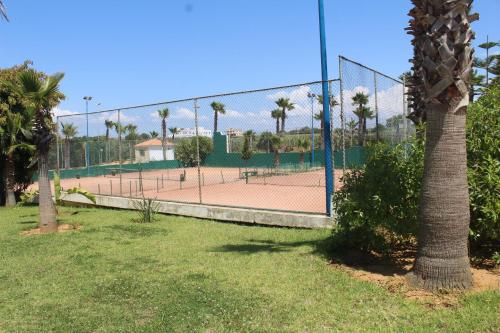 a tennis court with palm trees and a fence at Asilah Marina Golf, Appartement au calme in Asilah