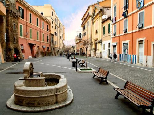 ulica z ławkami i fontanną w mieście w obiekcie Port House w mieście Civitavecchia