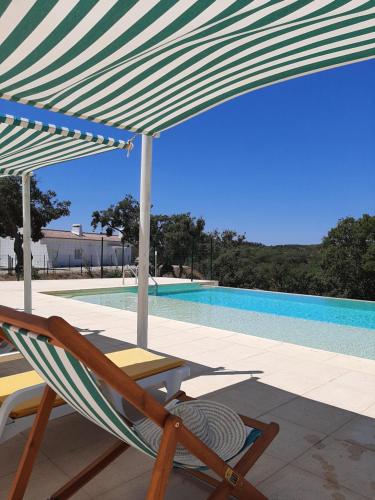 a chair under an umbrella next to a swimming pool at Monte Vale Manhãs by Hi Alentejo in São Bartolomeu da Serra