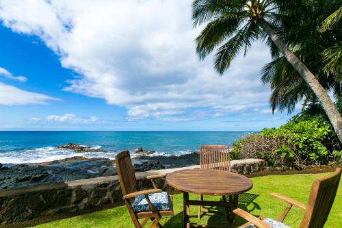 a table and chairs sitting on the grass near the ocean at Classic 3br Oceanfront Cottage - Alekona Kauai in Koloa