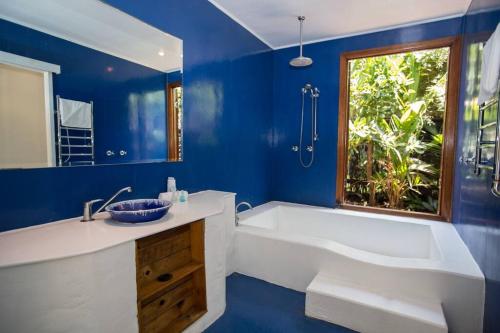 een blauwe badkamer met een bad, een wastafel en een raam bij Bev's on the Beach - Absolute Beachfront Cottage in Mission Beach