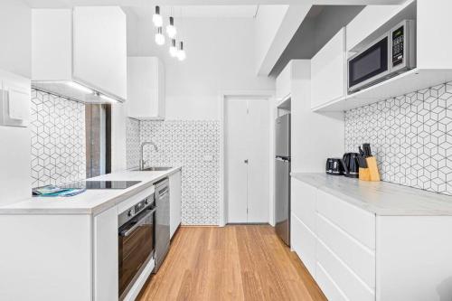 a white kitchen with white appliances and a wooden floor at Kings4 Self Catering in Sydney