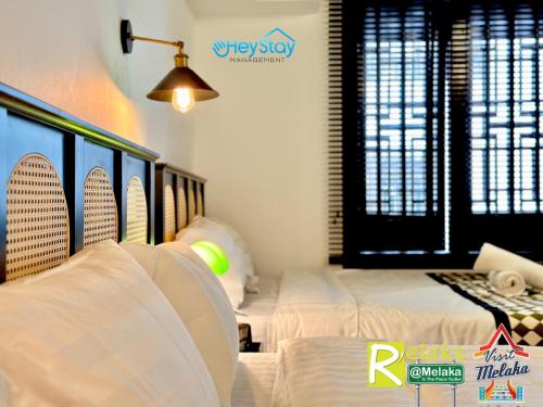 a bedroom with two beds with white sheets and a lamp at Wayfarer Guest House Jonker Street Melaka By Heystay Management in Melaka
