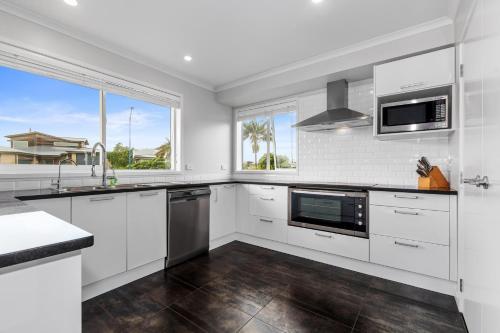 a kitchen with white cabinets and a large window at Shores Getaway - One Tree Point Holiday Home in One Tree Point