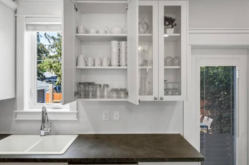 kuchnia z białymi szafkami, umywalką i oknem w obiekcie Comfort and joy w mieście Prince George