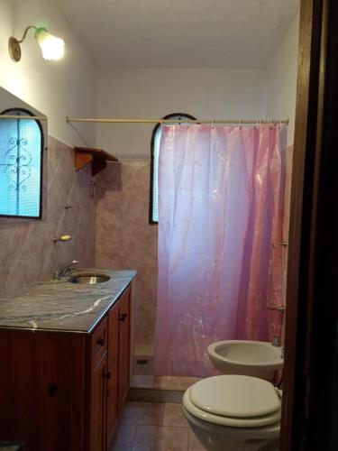 a bathroom with a pink shower curtain and a toilet at Cabaña Los Lirios in Huerta Grande