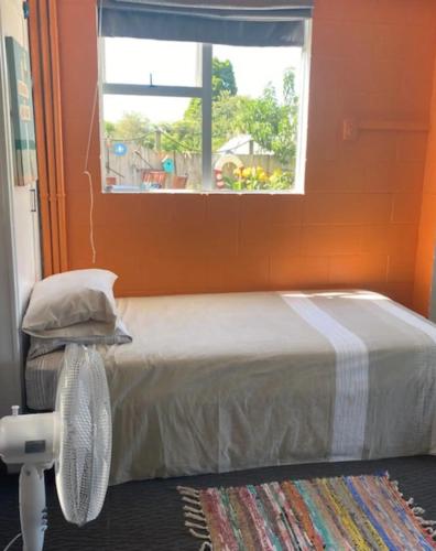a bedroom with a bed with an orange wall and a window at Corotime ~ Boat Parking ~ Pet Friendly in Coromandel Town