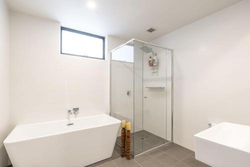 La salle de bains blanche est pourvue d'un lavabo et d'une douche. dans l'établissement Fayes Coastal Nest, à Kiama