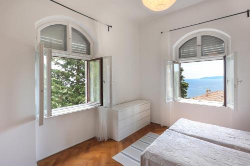 a white bedroom with two windows and a bed at Splendid View apartment Opatija in Opatija