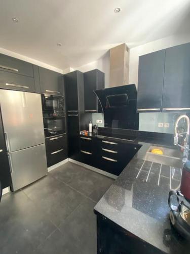 une cuisine avec des armoires noires et un réfrigérateur en acier inoxydable dans l'établissement Maison charme 7 min Paris jardin, à Courbevoie