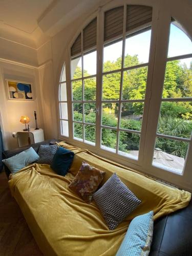 - un canapé avec des oreillers dans une chambre avec des fenêtres dans l'établissement Maison charme 7 min Paris jardin, à Courbevoie